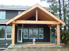 a small child standing in front of a large house with wood framing on the porch