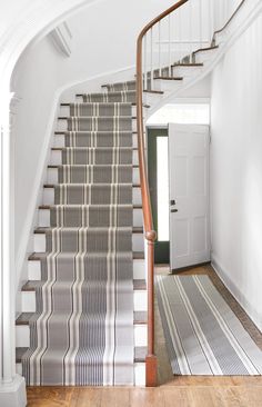 a staircase with striped carpet and wooden handrails in a white house, leading up to the second floor