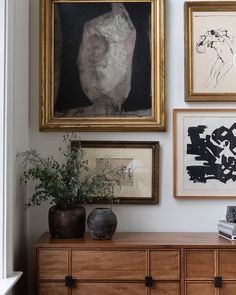 several framed pictures hang on the wall next to a dresser with vases and books