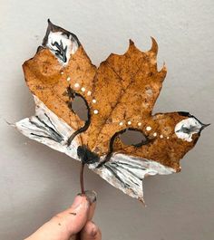 a person holding up a leaf that has been painted to look like a mask on it