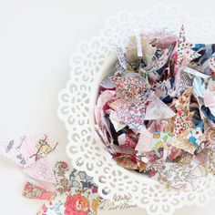 a white bowl filled with lots of different types of paper flowers on top of a doily