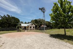 an old farm house with a windmill in the back ground and a dirt road leading to it