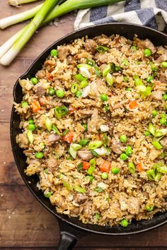 a skillet filled with rice and vegetables on top of a wooden table next to asparagus