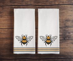 two white towels with yellow and black bees on them sitting on a wooden table next to each other