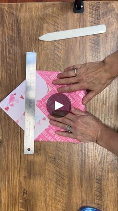 two hands are working on a piece of pink paper with a ruler next to it