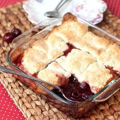 a glass dish filled with cherry pie on top of a red table cloth next to a white plate