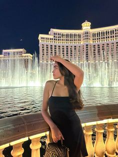 a woman standing in front of a fountain at night with her hand on her head