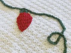 a crocheted strawberry is laying on top of a white blanket with green trim