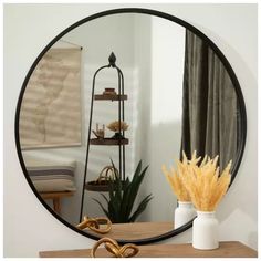 a round mirror sitting on top of a wooden table next to a vase filled with flowers