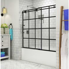 a bathroom with white tiles and black bars on the shower door, blue towels in the background