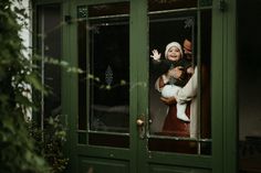 a man and woman holding a baby in front of a green door with glass panes