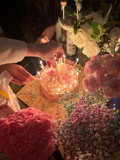 two people are lighting candles on a cake with flowers and confetti around it