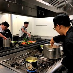 three people in a kitchen preparing food on top of stoves with pots and pans