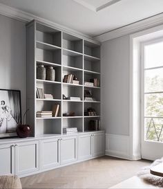 a living room filled with lots of white bookshelves next to a large window