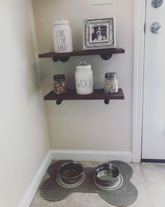 two dog bowls are sitting on the floor in front of some shelves with pictures and jars