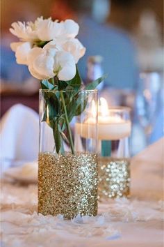 two vases filled with white flowers on top of a table covered in glitter and candles