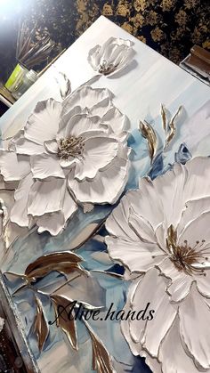 some white flowers are on a blue and gold table cloth with silver foil leaves in the center