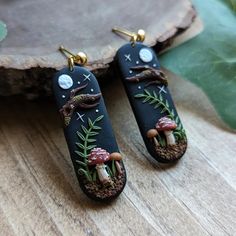 the earrings are decorated with small mushrooms and plants on black polymer, gold - plated earwires