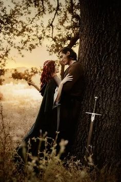 a man and woman standing next to each other in front of a tree with swords