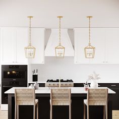 a kitchen with black and white cabinets, gold pendant lights over the island countertop