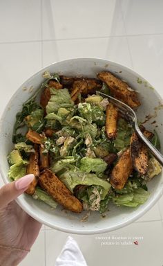 a person is holding a bowl of salad with fried potatoes and lettuce in it