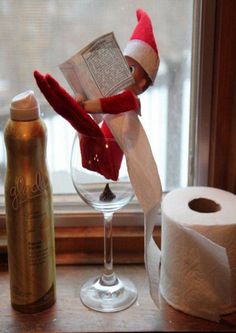 an elf reading a book next to toilet paper and a wine glass on a window sill