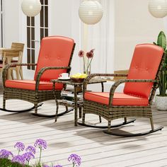 two chairs and a table on a deck with flowers in the foreground, next to potted plants