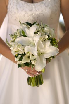 a woman in a wedding dress holding a bouquet of white lilies and greenery