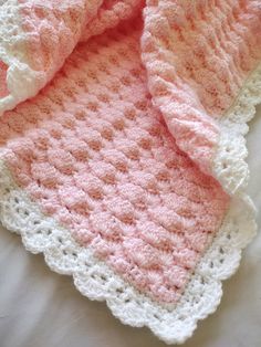 a pink and white crocheted blanket laying on top of a bed