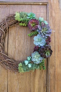 a wreath with succulents and greenery is hanging on a wooden door