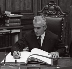 a man sitting at a desk in front of an open book with a pen and paper