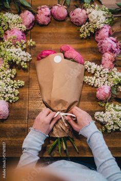 a person holding a bouquet of flowers on top of a wooden table with pink and white flowers