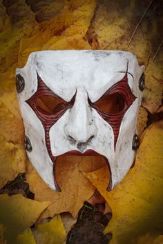 a white mask with red lines on it laying on top of some yellow and brown leaves