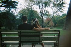 a man and woman sitting on a park bench looking at the trees in front of them