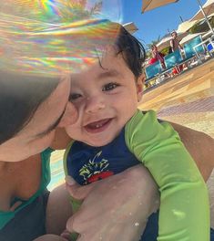 a woman holding a baby in her arms near the pool with an umbrella over it