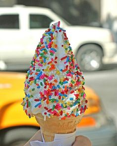 an ice cream cone with sprinkles on it being held by someone's hand