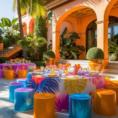 colorfully decorated tables and chairs in front of an orange building with palm trees on either side