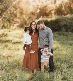 a man and woman holding two small children while standing in tall grass