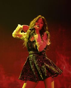 a woman in a short dress on stage with her hands up to her face and holding a microphone