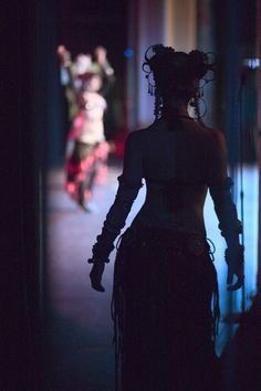 a woman walking down a dark hallway at night with her back turned to the camera