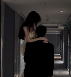 a man holding a woman in his arms while walking down a long hallway at night