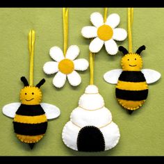 three felt bee ornament ornaments hanging on a green wall with yellow ribbon and white flowers