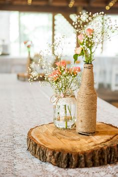 vases with flowers in them are sitting on a wooden slice at the end of a table