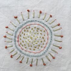 an embroidered circle with pins and needles in the center on a white cloth background that is stitched together