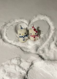 two hello kitty figurines sitting in the middle of a heart shaped snow bank