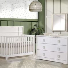 a white crib and dresser in a room with green walls, plants and mirror