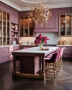 a large kitchen with purple cabinets and gold chandelier hanging from the center island