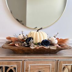 a wooden bowl filled with white pumpkins and blue flowers on top of a dresser