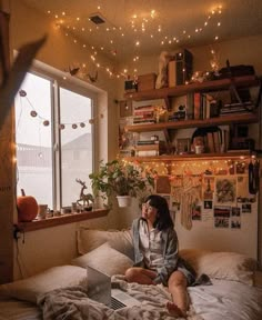 a person sitting on a bed with a laptop in front of them and lights strung from the ceiling