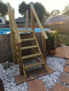 a wooden staircase next to an above ground swimming pool in a backyard with gravel and rocks